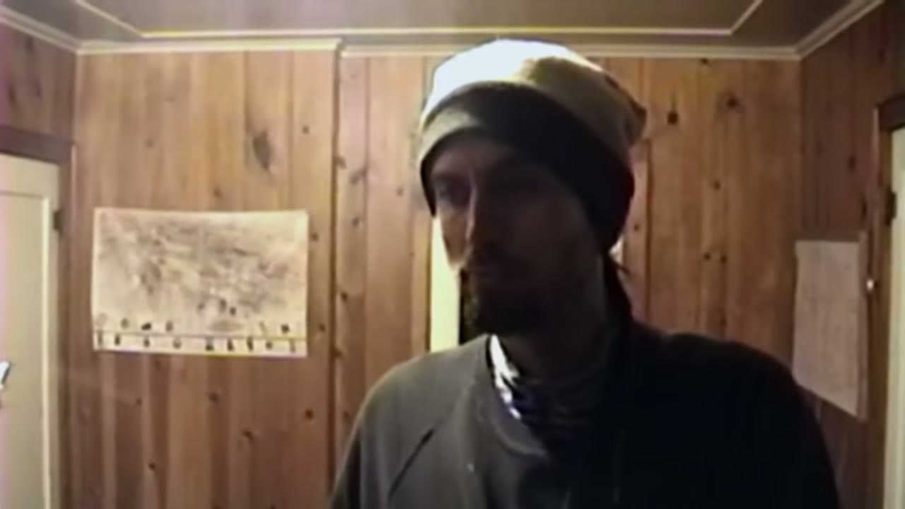 Jake Ferguson in archival footage, in a woollen hat in a wood-panelled room